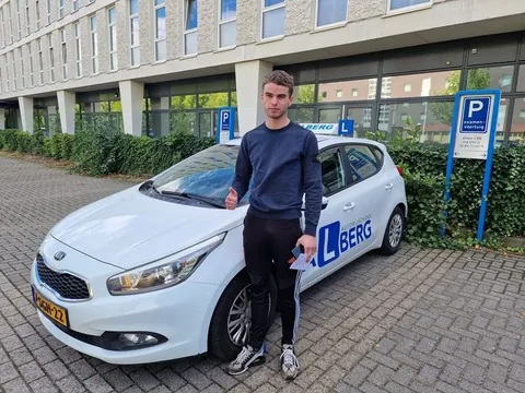 Geslaagde cursist poseert bij de lesauto van Autorijschool Valberg