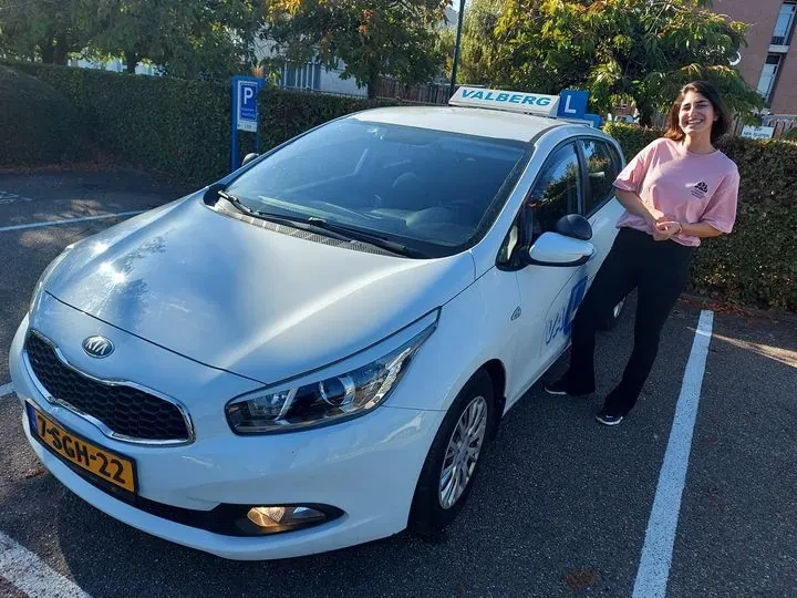 Geslaagde cursist poseert na het examen bij de lesauto